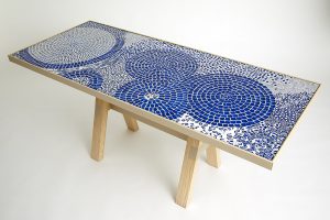 Mathilde Jonquière, mosaic artist, June 2023, original creation of a “Bleu d’ailleurs” table for Petit H, dimensions 1.70m x 070m. A veritable weave of intense blue, the color of the sky and the sea, which inspires dreaming and catches the light of the space. © Eugenia Sierko, Hermès